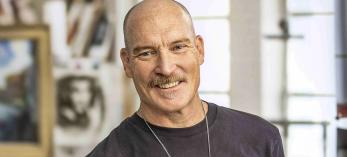 Photograph of Kevin Kibsey in studio setting holding a handful of paintbrushes is by Paul Markow.