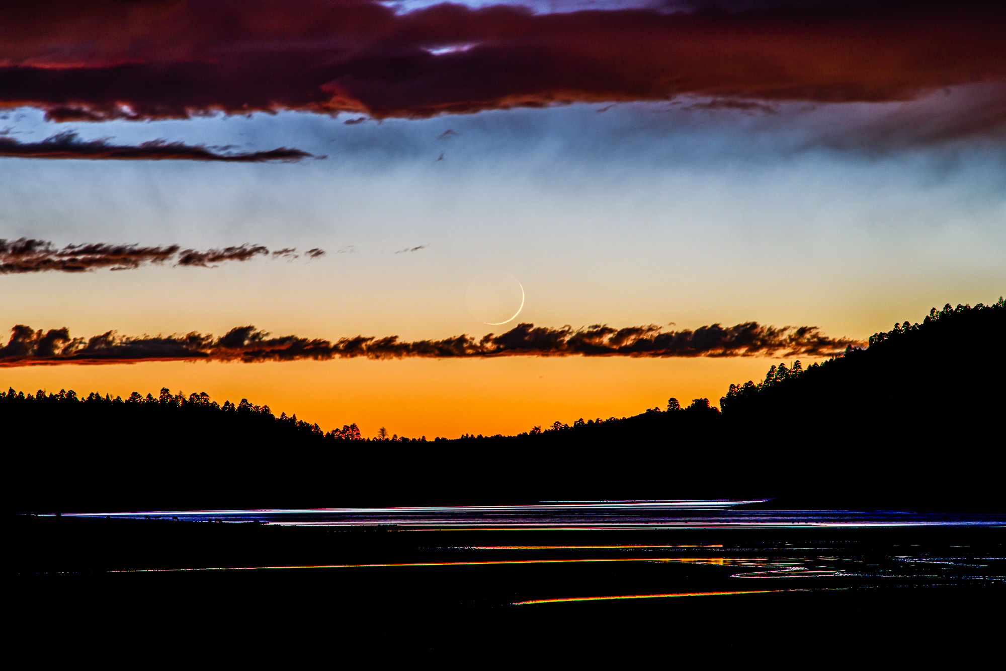 Photo by David Blanchard  |  A thin crescent Moon sets in the western twilight sky with colorful reflections on the waters of Upper Lake Mary near Flagstaff, Arizona.

Composite of two images: (1) sky and (2) foreground.
