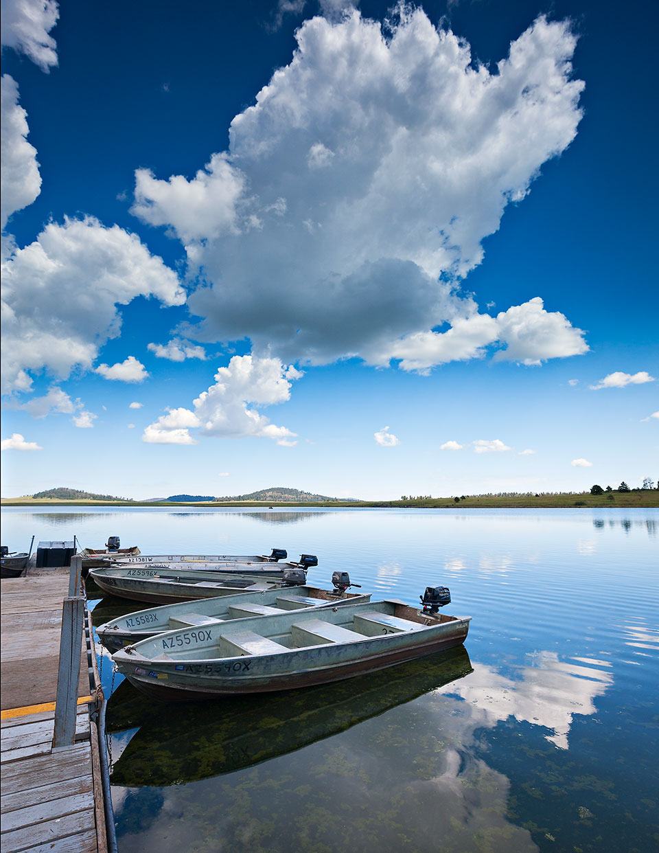 The placid water of Big Lake, the endpoint of a scenic drive from Eagar, mirrors docked boats and dramatic cloud formations. Photograph by Derek von Briesen.