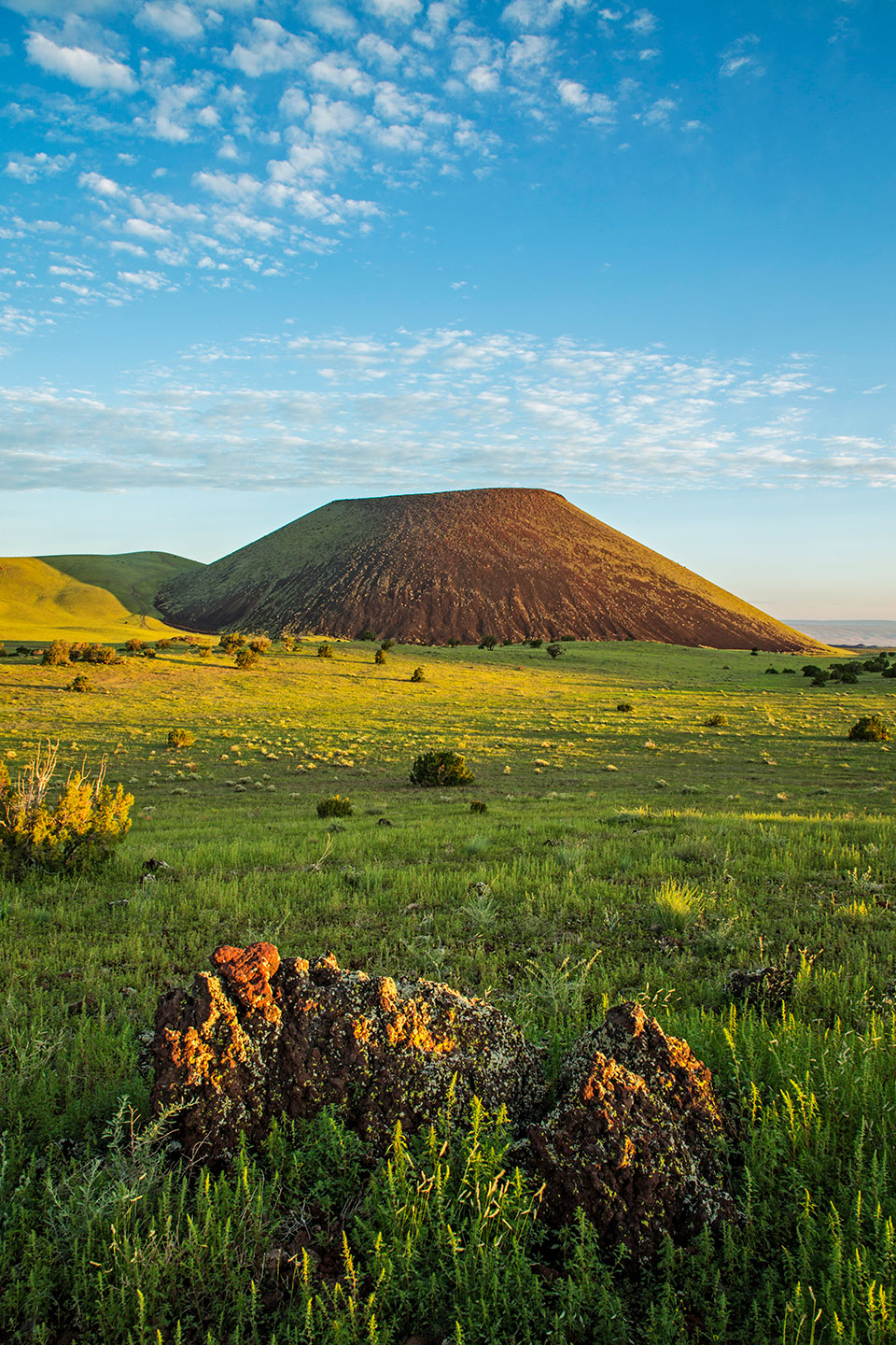 SP Crater, a cinder cone volcano north of Flagstaff, glows in early light amid grassy rangeland and volcanic rocks. Photograph by Tom Bean.