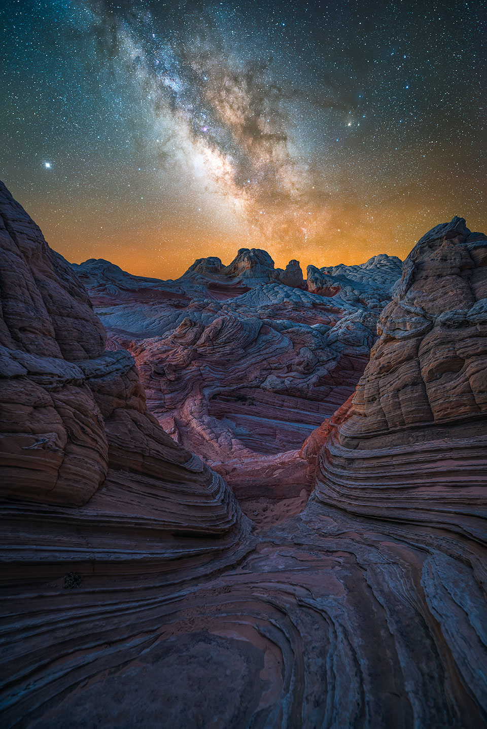 Starlight illuminates the strangely textured rocks of White Pocket, a remote destination on the Arizona Strip. The orange glow on the horizon is light pollution from cities far to the south. By Mike Sanchez