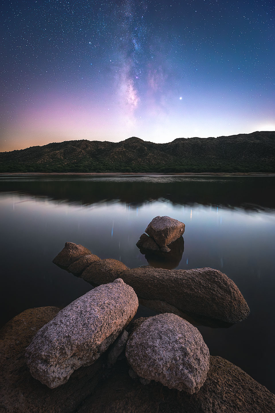 A cluster of granite boulders anchors a nighttime view from Bartlett Lake, a reservoir northeast of the Phoenix area. The faintness of the stars and the Milky Way is a result of light pollution from Phoenix. By Mike Sanchez