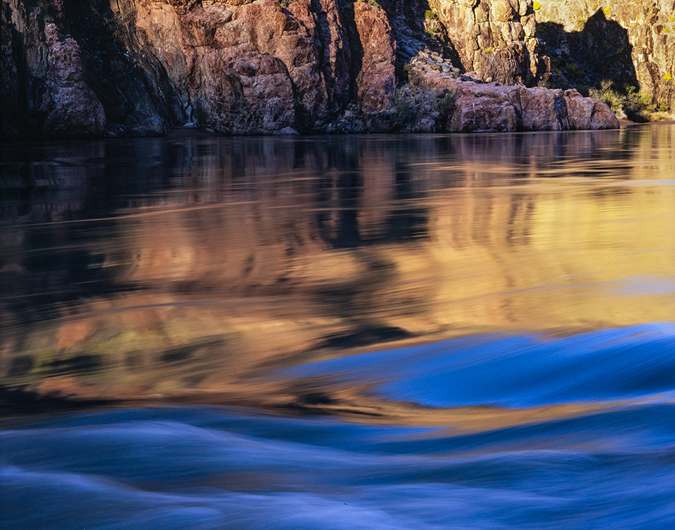 At the top of Granite Rapid, the Colorado River mirrors the cliffs of the Upper Granite Gorge. In this section of the Canyon, erosion-resistant rocks some 1.8 billion years old are exposed, creating larger rapids. By Gary Ladd