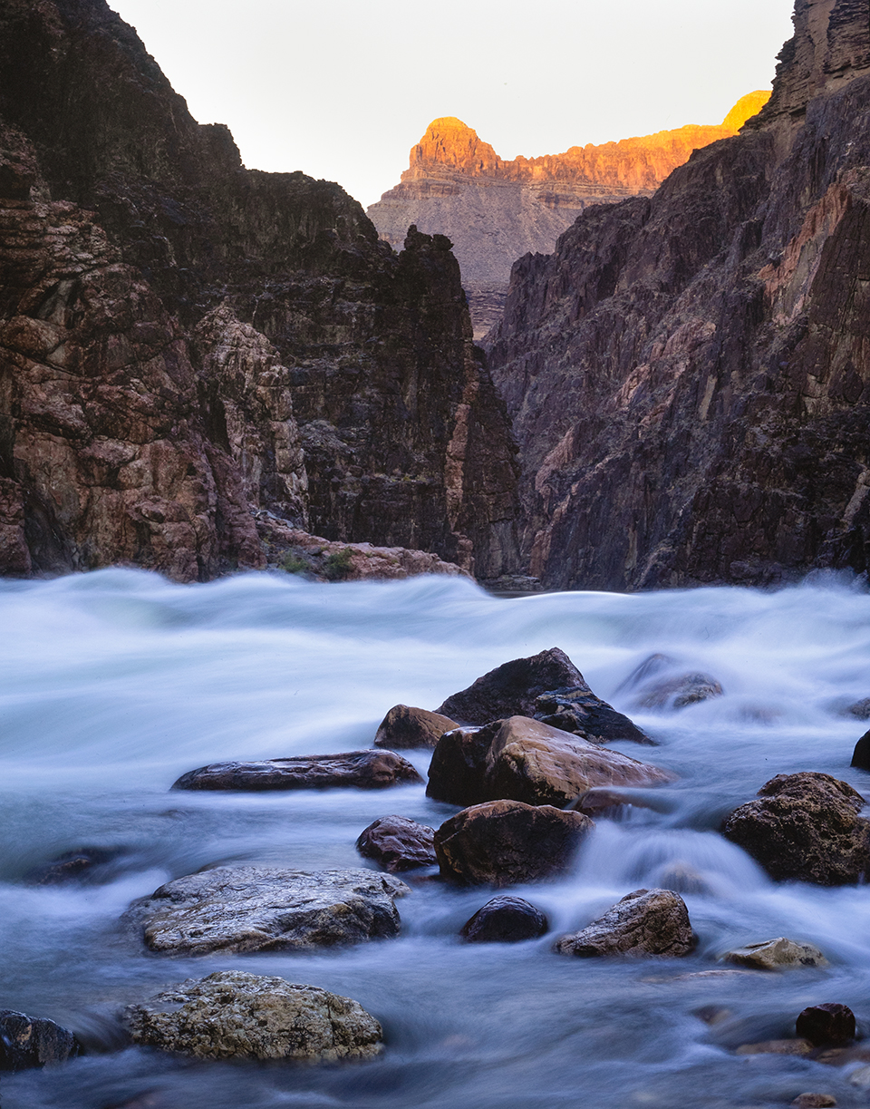 The Colorado flows over and around boulders in Granite Rapid, at the mouth of Monument Canyon, at sunset. Known for its massive waves and swift current, this rapid is a highlight of Canyon rafting trips. By Gary Ladd