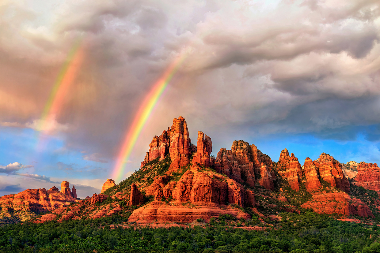 Amid falling rain from an isolated storm cell, a pair of rainbows appear over the sandstone buttes of Red Rock Country at sunset. In theory, all rainbows are double rainbows, but the secondary rainbow is often too faint to be seen. | Theresa Rose Ditson