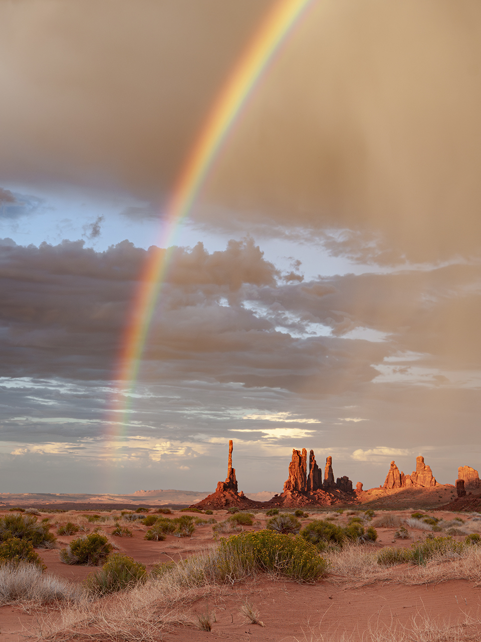 The Totem Pole (left) and Yei Bichei, two sandstone formations in the Navajo Nation’s Monument Valley, reach toward a rainbow and a cloudy sky. In Navajo traditions, rainbows are seen as pathways used by holy spirits. | Doug Koepsel