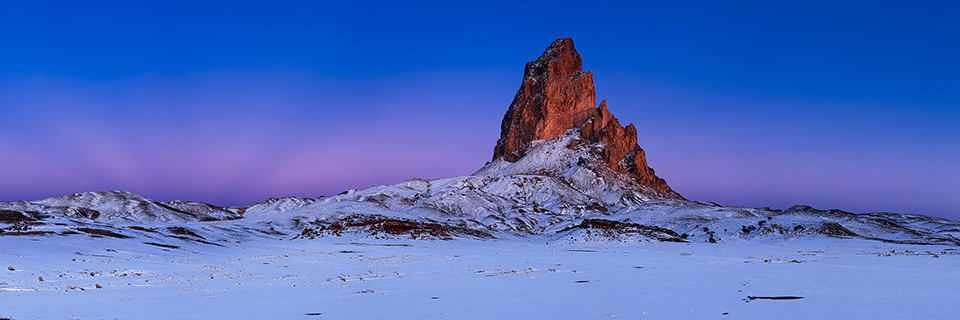 Agathla Peak rises above the snow covered landscape at twighlight near Monument Valley. By Dennis Tromburg