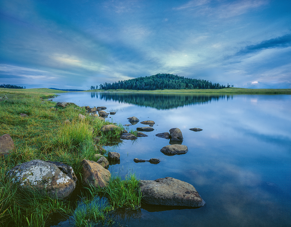 After sunset, the calm water of Crescent Lake, in the White Mountains, reflects the evergreens on a nearby volcanic knoll. Located just north of Big Lake, this reservoir is known for its crystal-clear water and for attracting deer, elk, foxes and other wildlife. Jack Dykinga