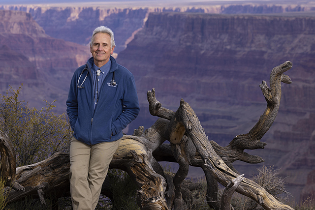 Tom Meyers leans against a fallen dead tree at the edge of the Grand Canyon. By John Burcham