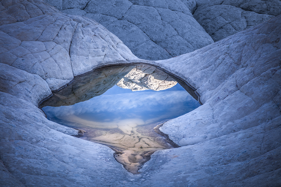 A shallow pool in the textured “brain rock” of White Pocket, in the Vermilion Cliffs of Northern Arizona, mirrors sky and stone in early morning light. A high-clearance, four-wheel-drive vehicle is required to reach this extremely remote site. Suzanne Mathia