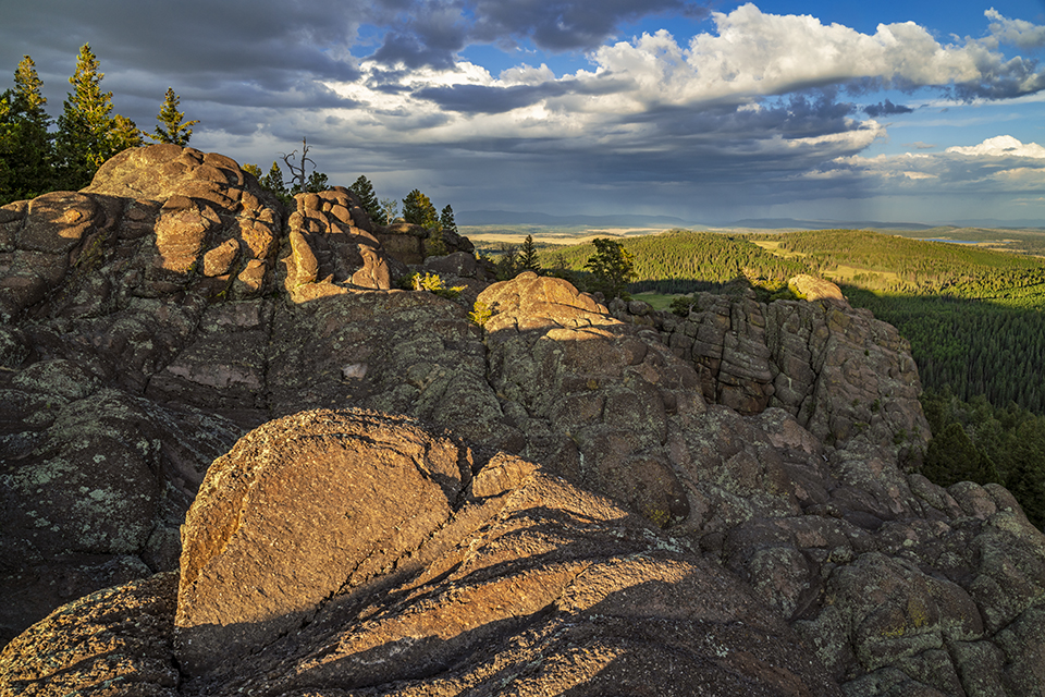 Long shadows fall on volcanic rock formations along the East Baldy Trail, in the White Mountains of Eastern Arizona, as a distant thunderstorm rages. East Baldy is one of two main routes that approach the summit of Mount Baldy, the White Mountains’ highest point. By Laurence Parent