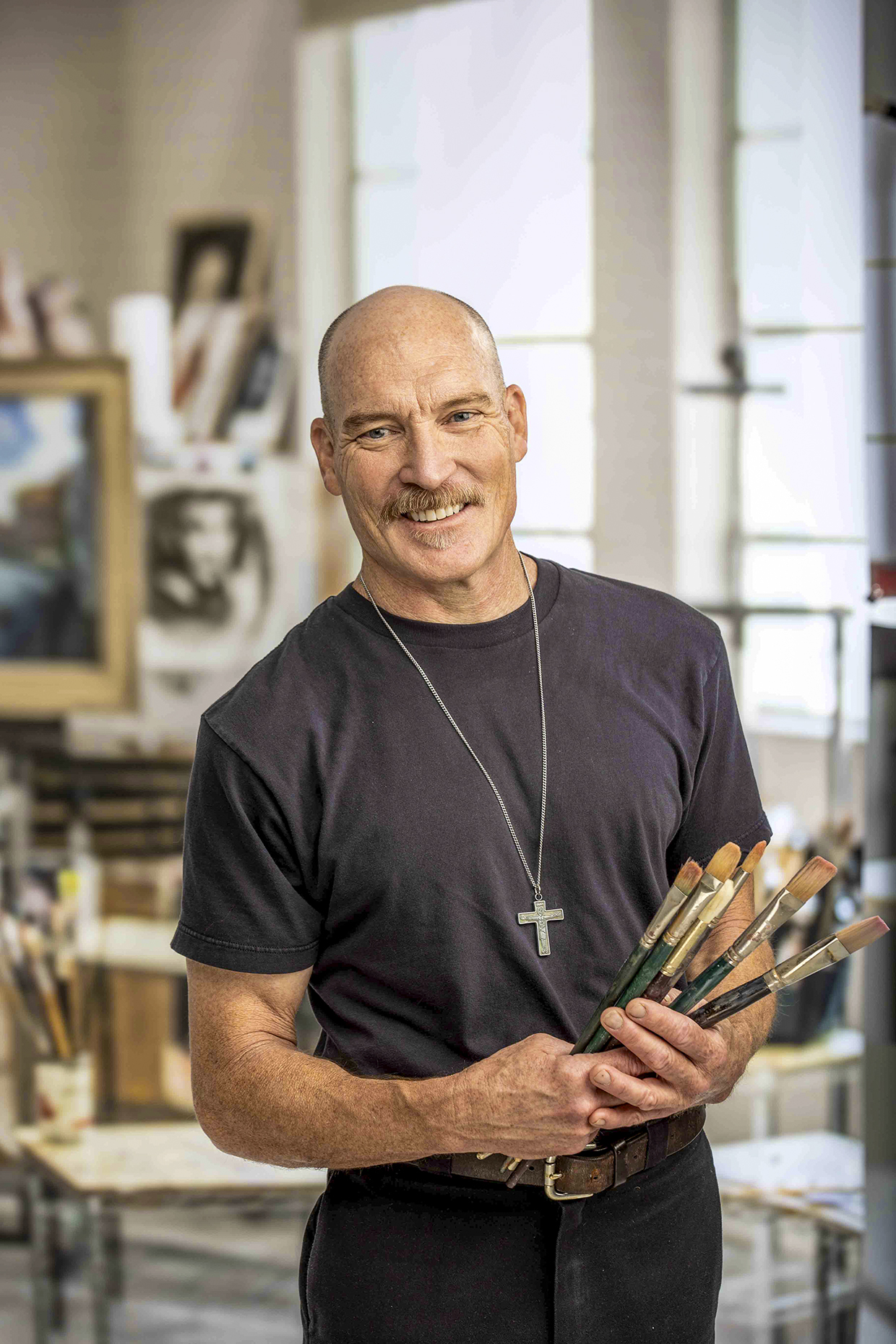 Photograph of Kevin Kibsey in studio setting holding a handful of paintbrushes is by Paul Markow.