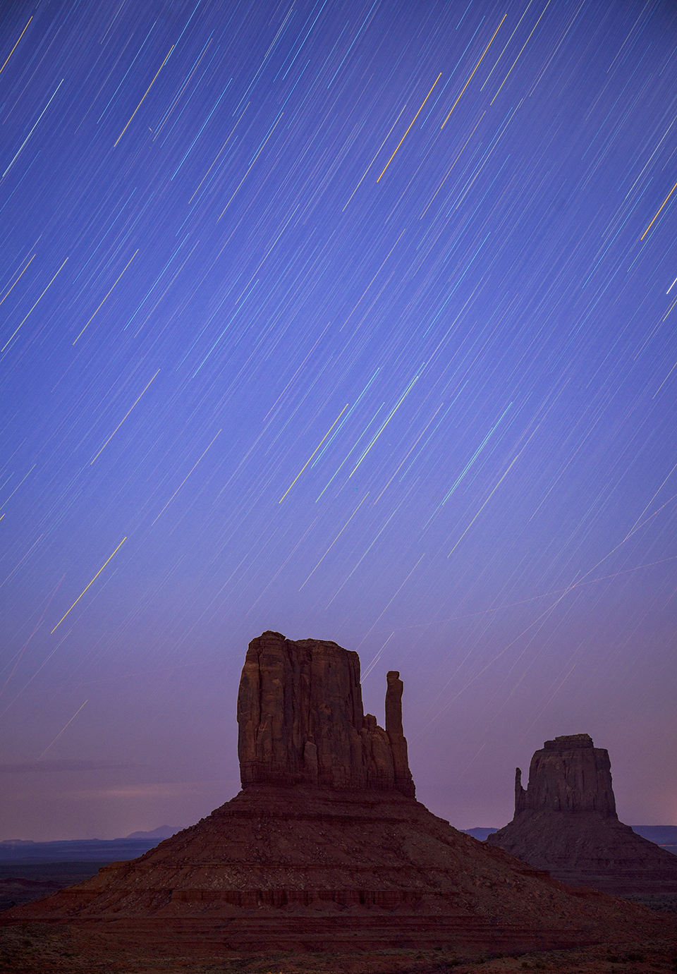 Stars make trails across the night sky in a long-exposure photo of the Mittens in Monument Valley. | Kerrick James