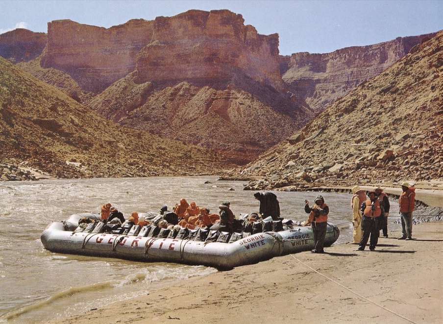 On the Colorado River in the Grand Canyon, a group boards a large, inflatable raft with Georgie White's name emblazoned on each side. By Josef Muench