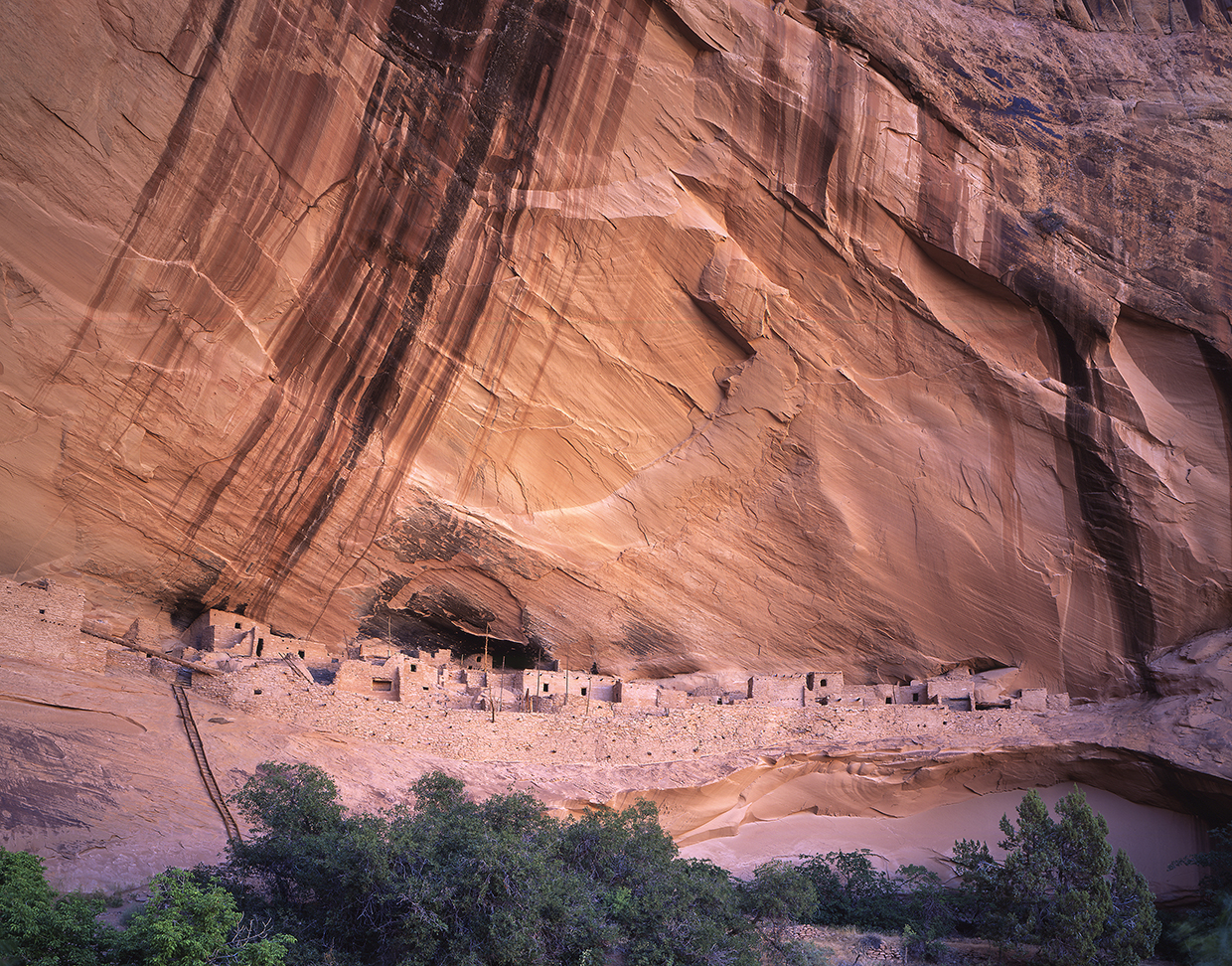 Keet Seel ruins sits perched on a cliff beneath a streak-stained sheer canyon wall. By Laurence Parent
