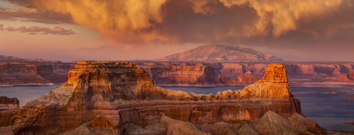 Storm clouds swirl at sunset over Gunsight Butte, Lake Powell and distant Navajo Mountain from Alstrom Point at Glen Canyon National Recreation Area.| Photograph by Larry Lindahl