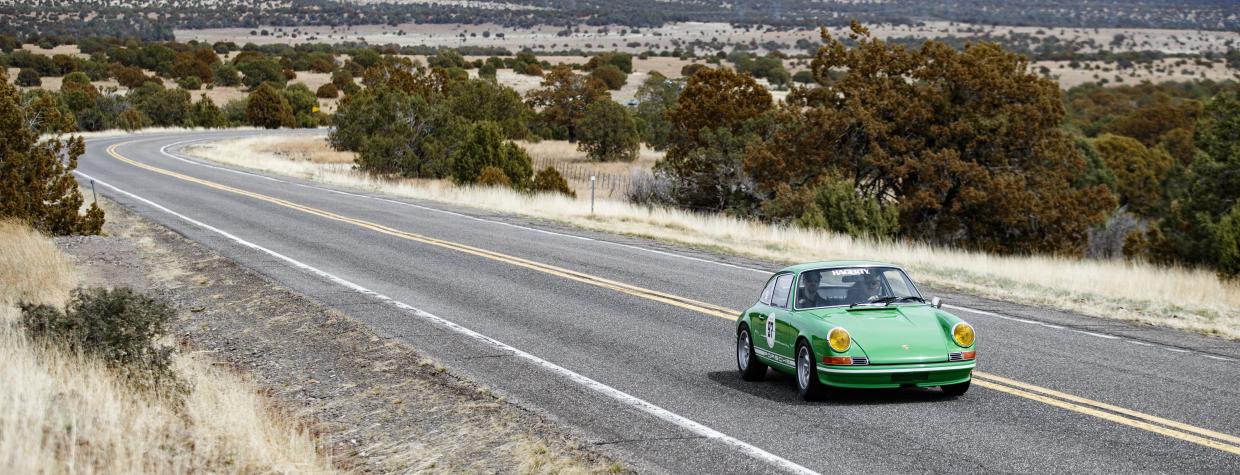 A green sports car cruises down a highway.