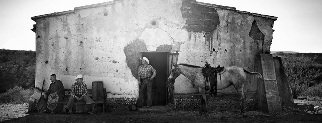Cowboys stand in front of a ranch building in this black and white photograph