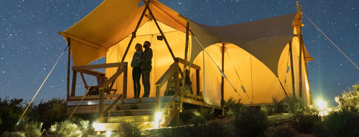 Campers look at a starry sky from beneath a canvas tent. 