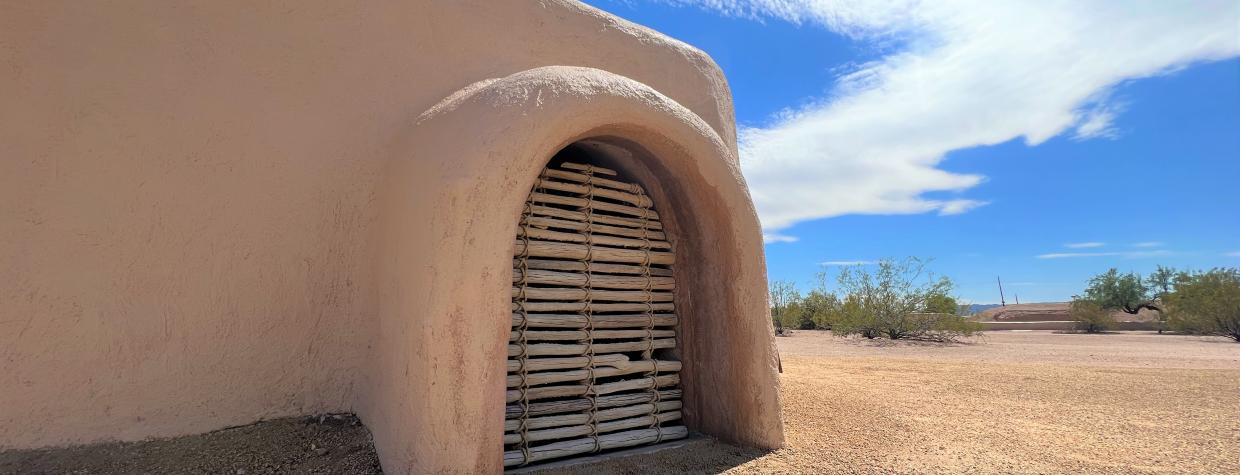 The adobe walls of S'edav Va'aki Museum are shown against a bright blue sky with whispy white clouds.