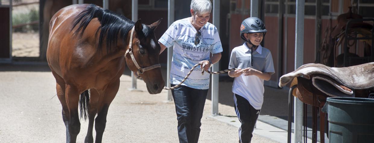 A trainer and young client walk alongside a dark brown horse. 