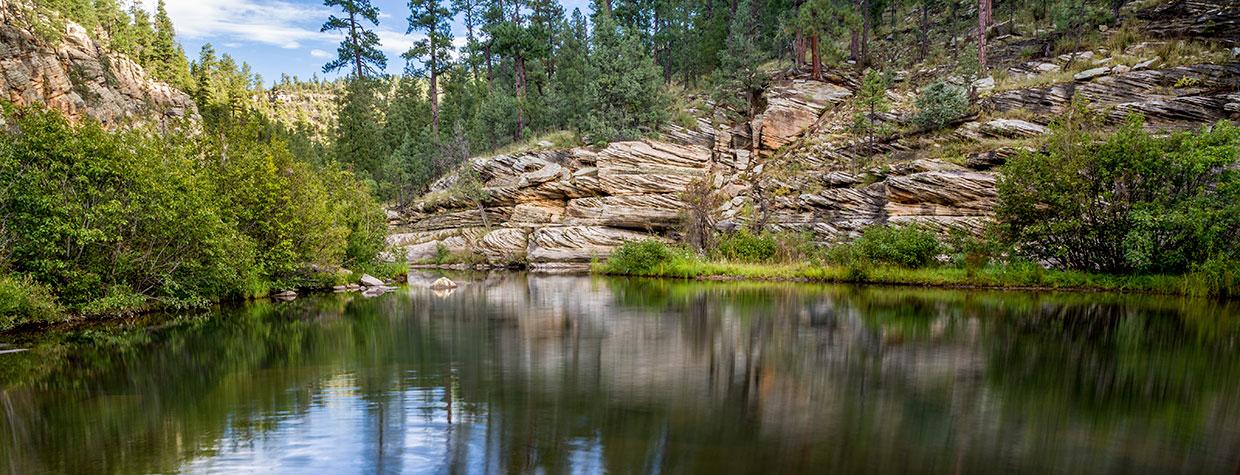 The calm water of East Clear Creek mirrors trees along the Kinder Crossing Trail. By Rebecca Wilks