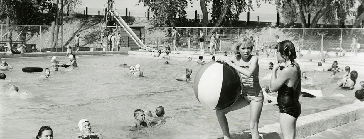 BW photo of two girls with giant beach ball at edge of the pool at Tempe Beach, which is occupied by several other people. Photograph: TEMPE HISTORY MUSEUM