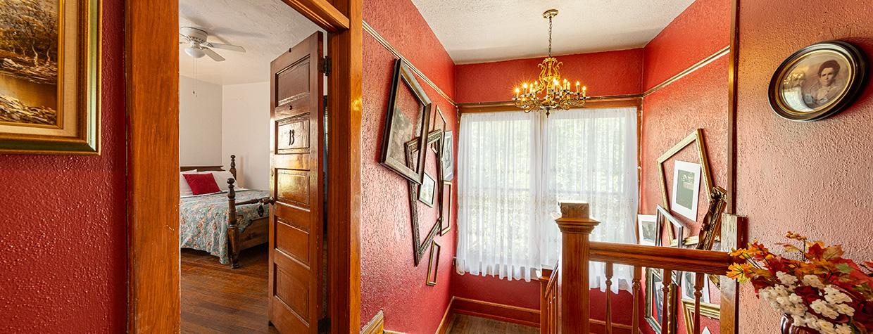 Upstairs hallway, painted red and showing the inside of a guest room and adjacent staircase at the Oliver House. By Steven Meckler