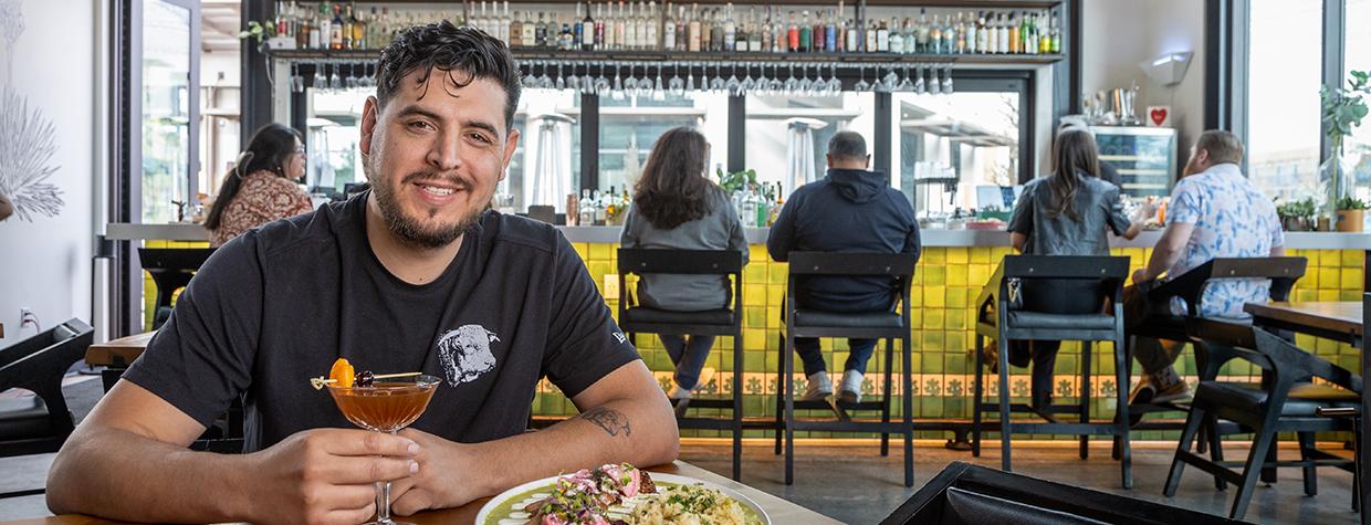 Armando Hernandez with food and drink at a table in Cocina Chiwas with the bar in the background. By Paul Markow 