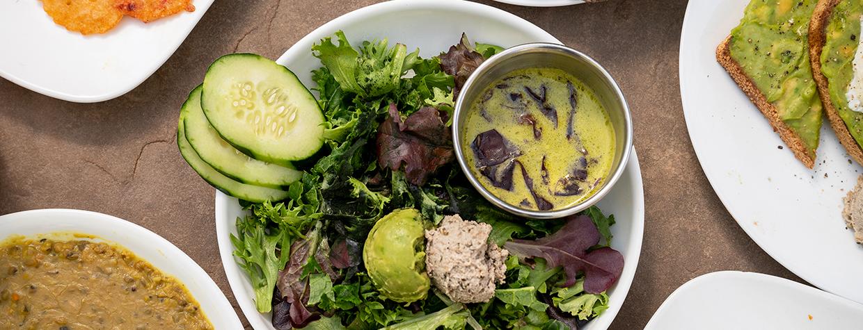 A green salad garnished with cucumbers, guacamole, tuna salad, bread and dressing is the centerpiece of assorted plates that include avocado toast and beans. By Dawn Kish