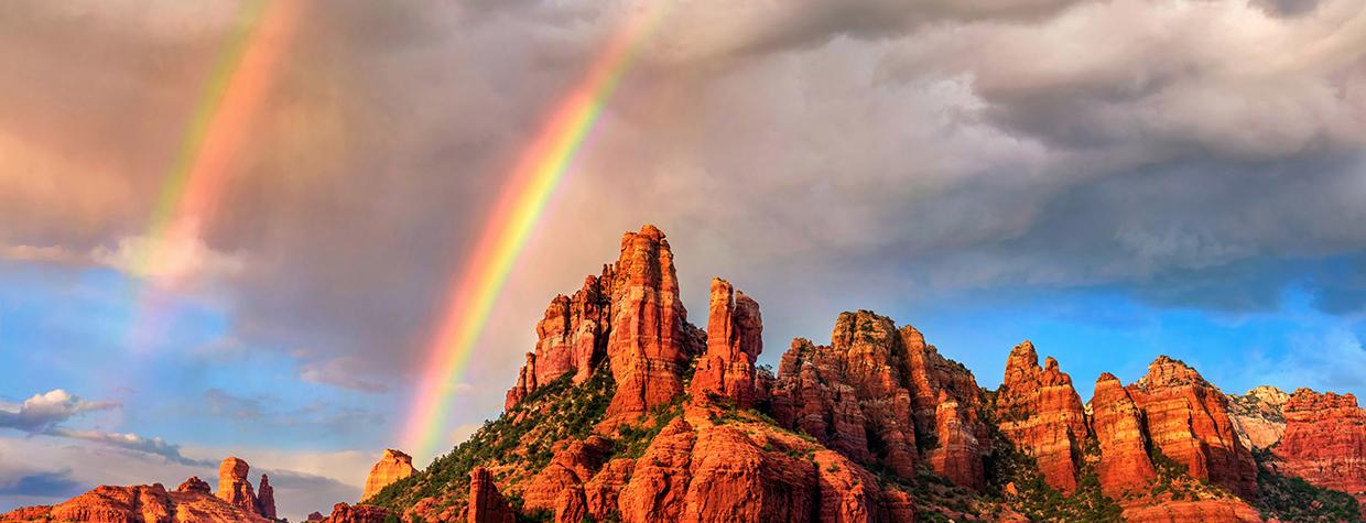 Amid falling rain from an isolated storm cell, a pair of rainbows appear over the sandstone buttes of Red Rock Country at sunset. In theory, all rainbows are double rainbows, but the secondary rainbow is often too faint to be seen. | Theresa Rose Ditson