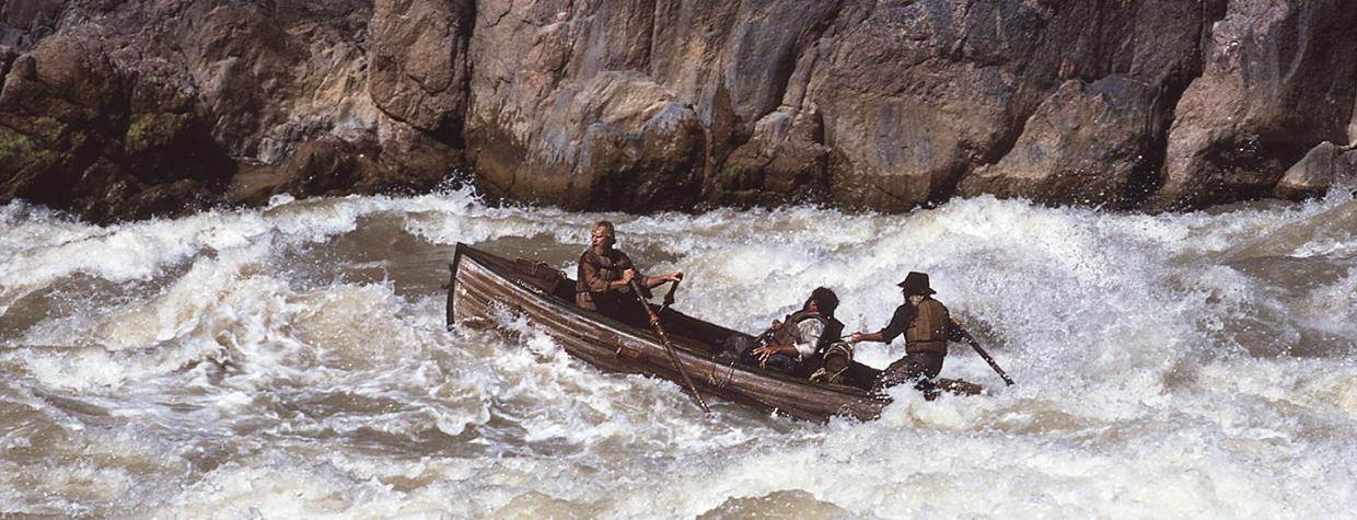 Bruce Simballa (on oars) and Kenton Grua (steering) guide an authentic Whitehall boat, the kind used by John Wesley Powell’s party, through the Grand Canyon’s Granite Rapids for an Imax film in 1984. Powell’s group portaged these rapids, but modern boatmen have the skills and experience to run these boats through the Canyon’s largest rapids. By Rudi Petschek