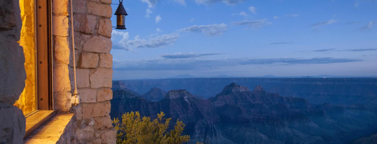 The edge of a building appears in the left of an image that is dominated by the Grand Canyon under an evening sky. 