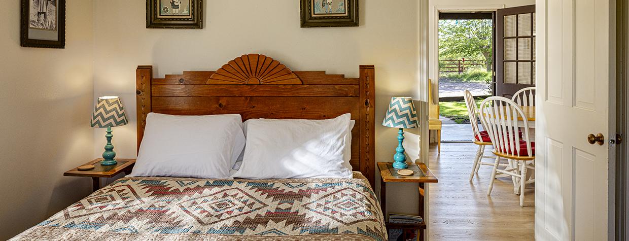 Interior of cottage bedroom shows view through front room through open door to outside. By Steven Meckler