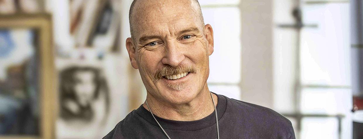 Photograph of Kevin Kibsey in studio setting holding a handful of paintbrushes is by Paul Markow.
