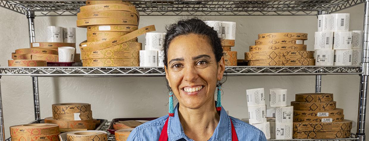 Amy Valdés Schwemm spoons mole powder into dozens of tins, backed by ingredient racks. By Steven Meckler