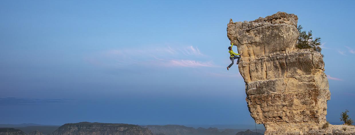 John Burcham captured this dramatic photo of a rock climber nearing the overhang at the top of rocky outcrop.