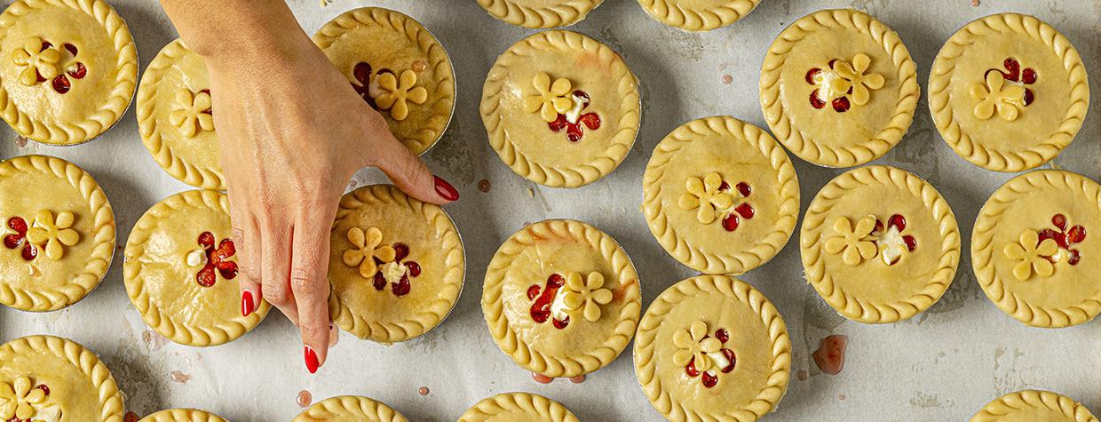 Photograph of a hand reaching for a small, decorative pie among dozens is by Steven Meckler