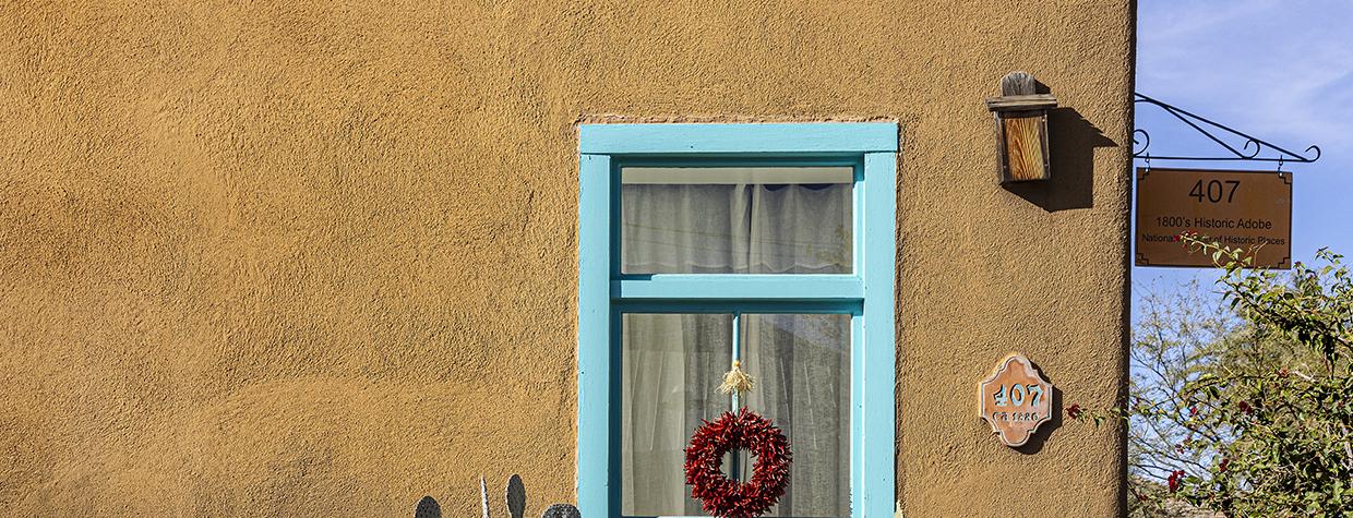A building in Tucson's El Presidio barrio shows off a brightly-painted window frame flanked by two large light green ceramic pots housing prickly pear cactus. By Steven Meckler