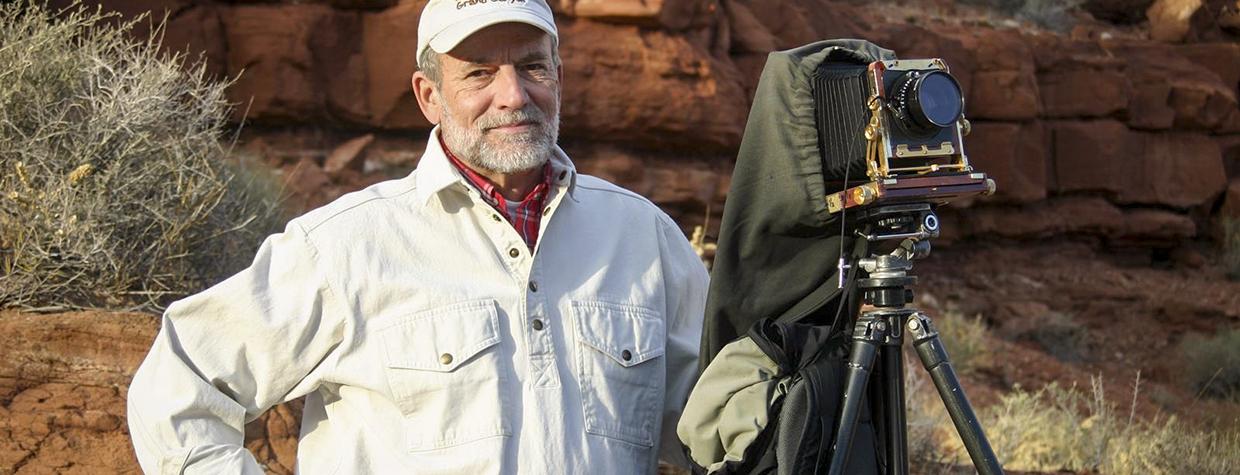 Portrait of Gary Ladd with 4x5 camera against a backdrop of red rocks is by Renee Roundtree.