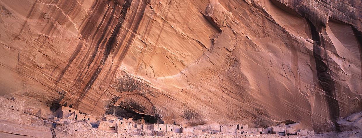 Keet Seel ruins sits perched on a cliff beneath a streak-stained sheer canyon wall. By Laurence Parent