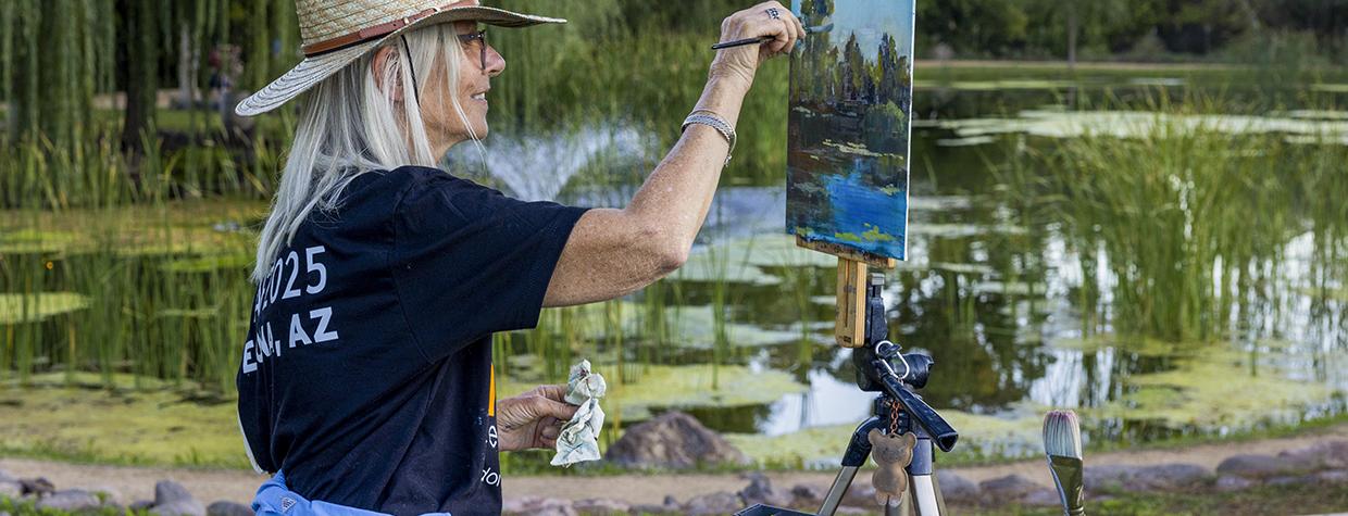 Photograph of a woman painting from an easel outside by a pond is by John Burcham