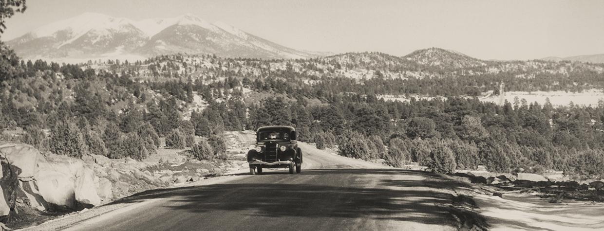 With the snowy San Francisco Peaks in the background, a motorist heads west on the stretch of Route 66 between Williams and Parks, likely in the 1930s or ’40s. | NORMAN G. WALLACE/ARIZONA HISTORICAL SOCIETY