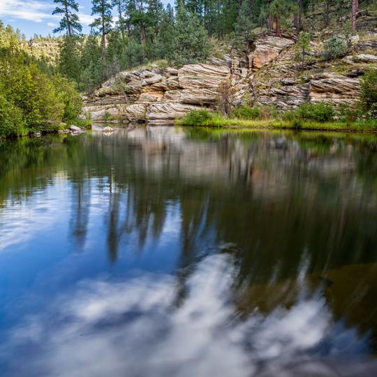 The calm water of East Clear Creek mirrors trees along the Kinder Crossing Trail. By Rebecca Wilks