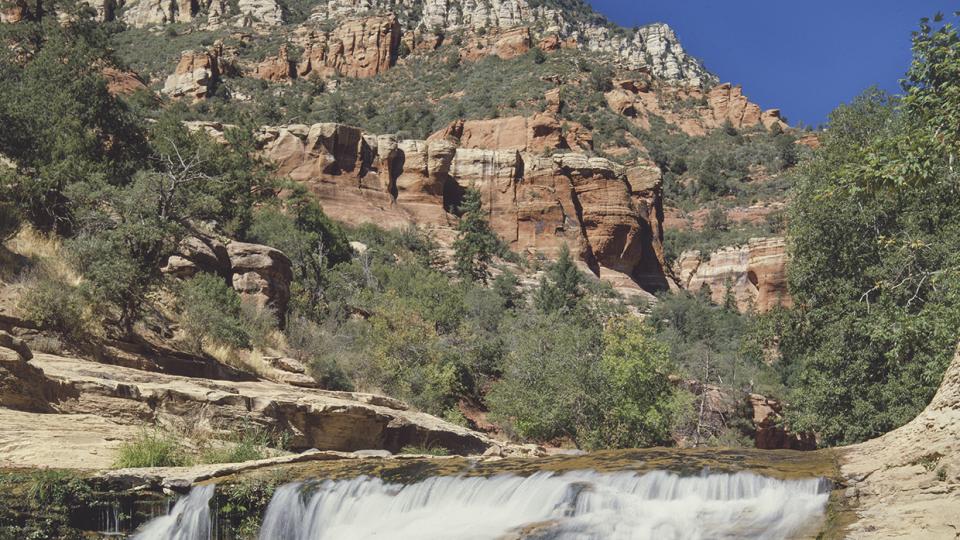 The clear water of Oak Creek tumbles over a small waterfall in the Slide Rock area of Oak Creek Canyon, near Sedona. At the time this photo was made, the Slide Rock area had not yet become an Arizona state park; it received that designation in 1987. By Josef Muench