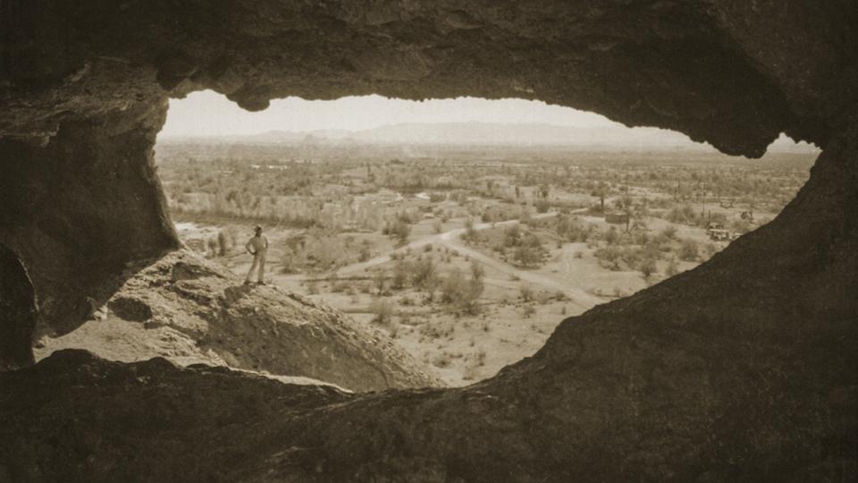 A hiker admires the view from Hole-in-the-Rock, the centerpiece of present-day Papago Park in Phoenix and Tempe, in an undated postcard photo. The site became Papago Saguaro National Monument in 1914, but it lost that designation less than two decades later. | Phoenix Public Library