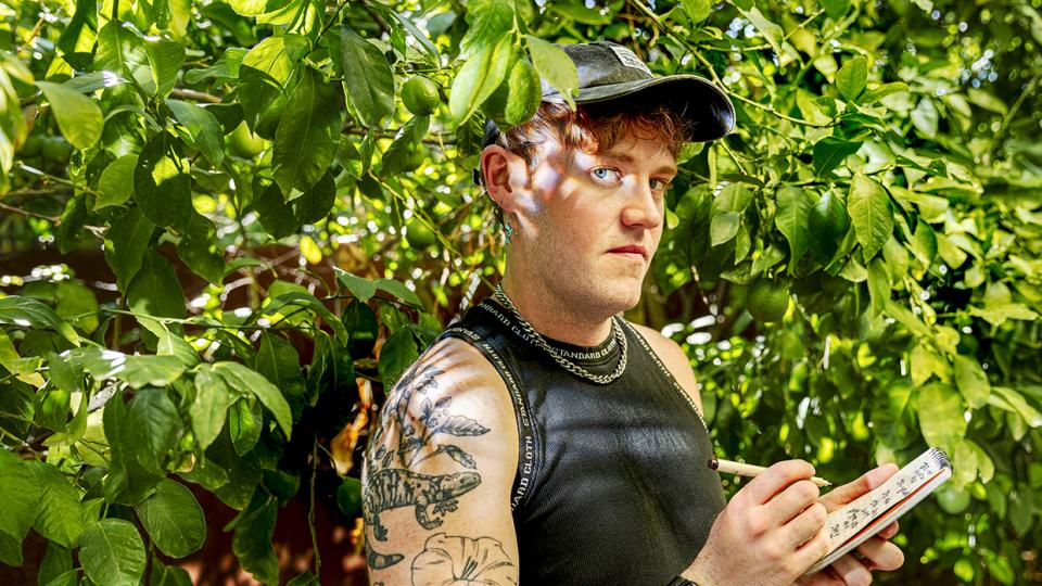 Photograph of Jonathan T. Bailey standing in green foliage while writing in a notepad is by Steven Meckler.