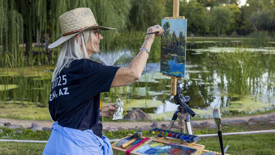 Photograph of a woman painting from an easel outside by a pond is by John Burcham