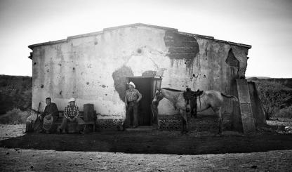 Cowboys stand in front of a ranch building in this black and white photograph