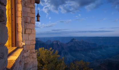 The edge of a building appears in the left of an image that is dominated by the Grand Canyon under an evening sky. 